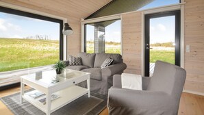 Ein modernes Wohnzimmer mit einer grauen Couch, einem weißen Couchtisch und einem großen Fenster mit Blick auf ein grünes Feld.