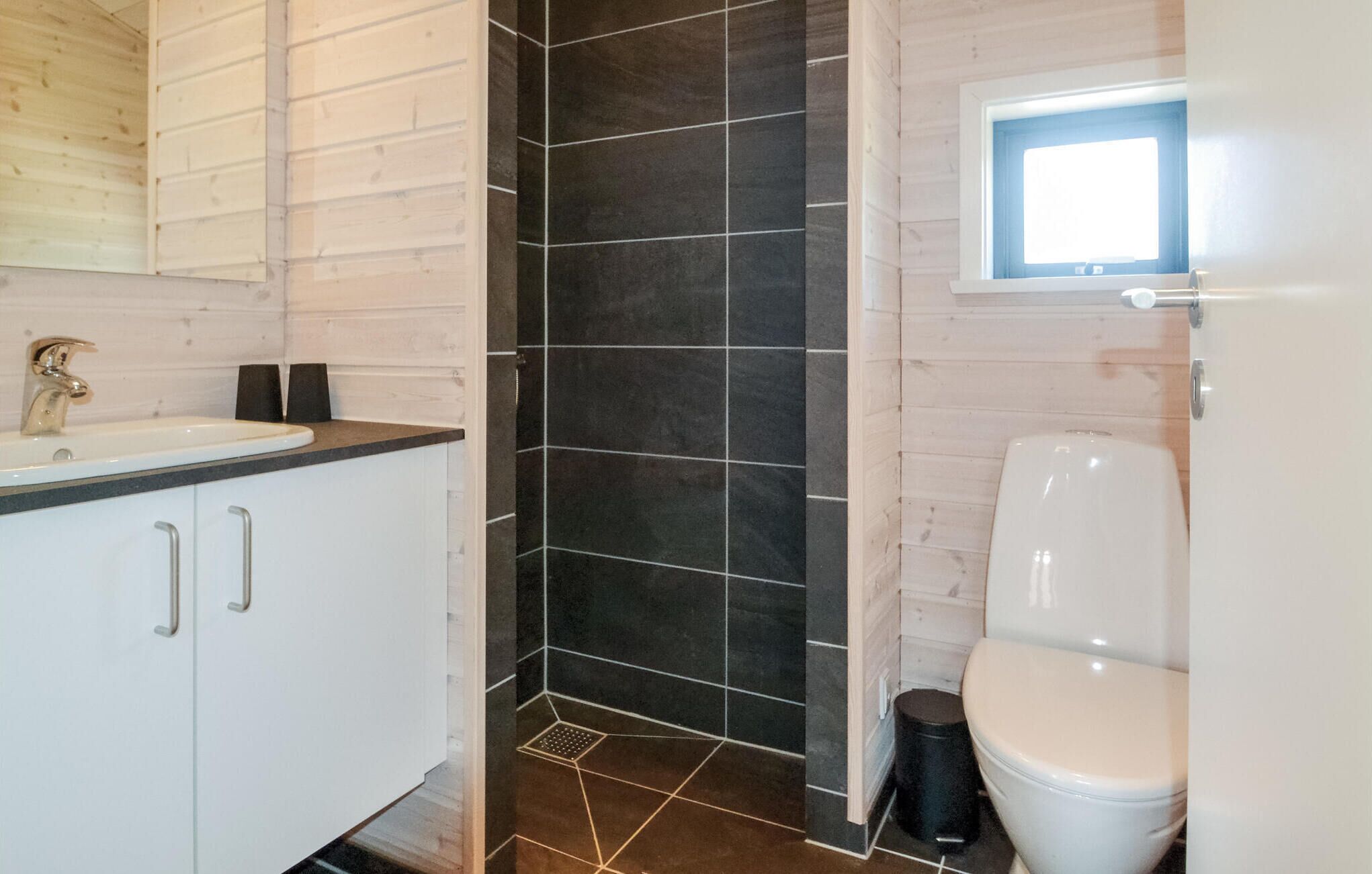 Une salle de bain avec un lavabo blanc, une douche carrelée de couleur foncée et des toilettes.