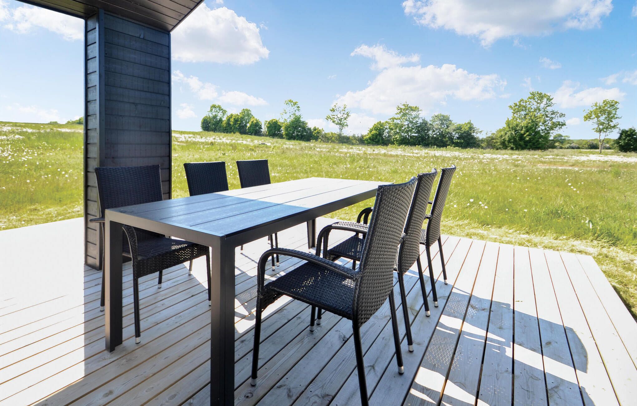 An outdoor deck with a table and chairs, overlooking a grassy field and trees.
