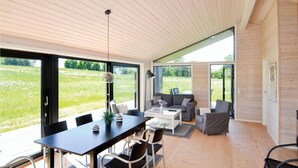 Ein modernes Interieur mit Essbereich, Sofagarnitur und großen Fenstern mit Blick auf ein grünes Feld.