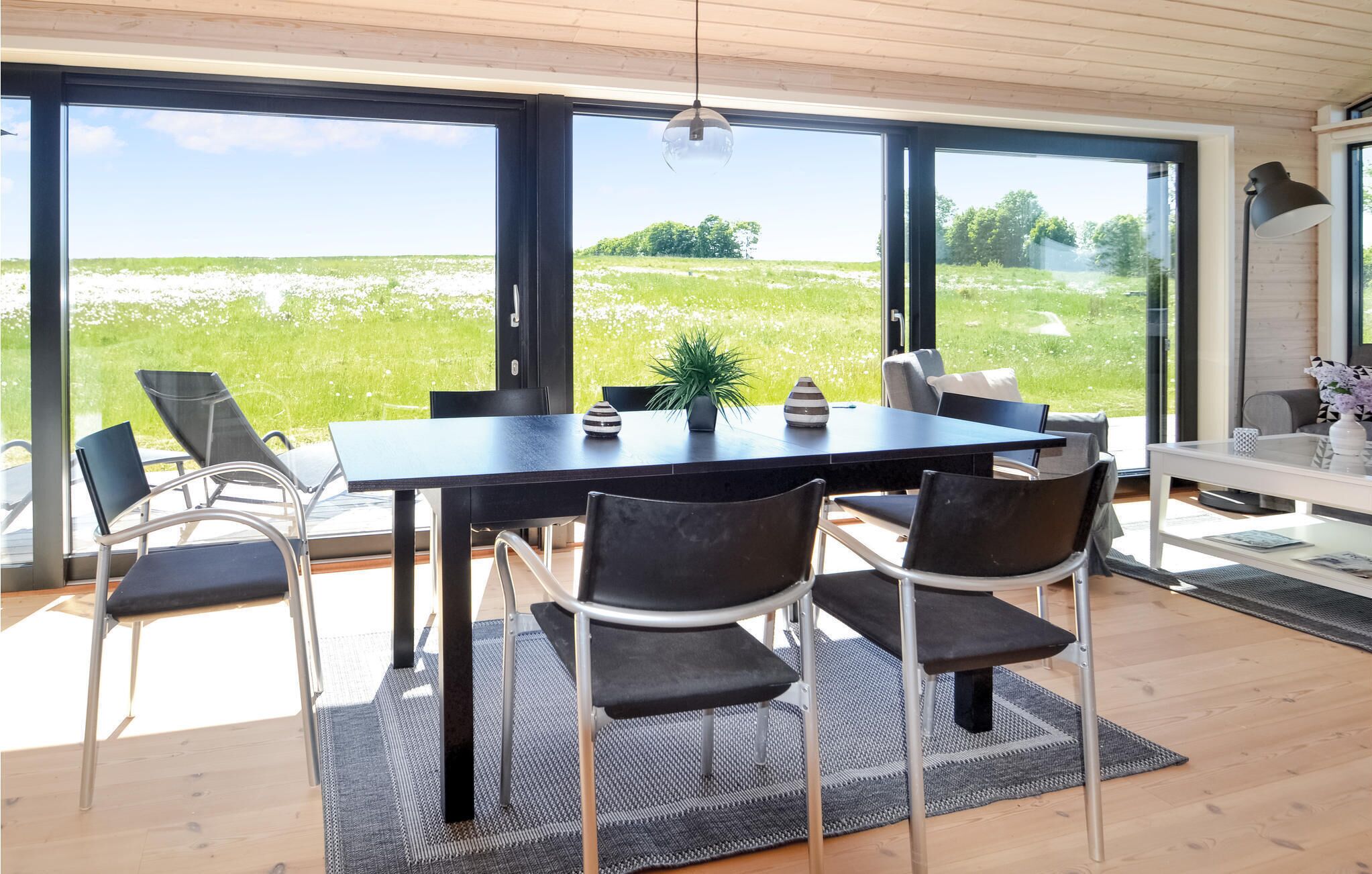 Un espace repas moderne avec une grande table et des chaises, de grandes fenêtres donnant sur un champ verdoyant.