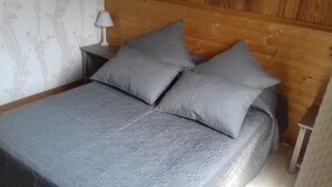 A bed with grey bedding and pillows, a wooden headboard, and a nightstand with a lamp.