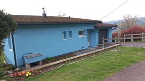 A blue house with a tiled roof, a small porch, and a flower bed.