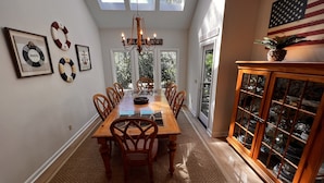 A dining room with a long wooden table, chairs, a chandelier, and a cabinet with glass doors. - Spacious Sea Pines home - professionally decorated - Private Pool/Hot Tub (Hilton Head Island)
