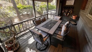 A covered outdoor seating area with a table and chairs, surrounded by a wooden deck and a view of trees. - Spacious Sea Pines home - professionally decorated - Private Pool/Hot Tub (Hilton Head Island)
