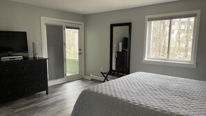 Ein Schlafzimmer mit einem Bett, einem Schminktisch, einem Fernseher, einem Spiegel und einer Tür, die auf einen Balkon führt.