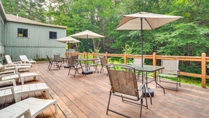 Eine Holzterrasse mit Außenmöbeln, darunter Lounge-Stühle und Tische, umgeben von üppiger Bepflanzung.