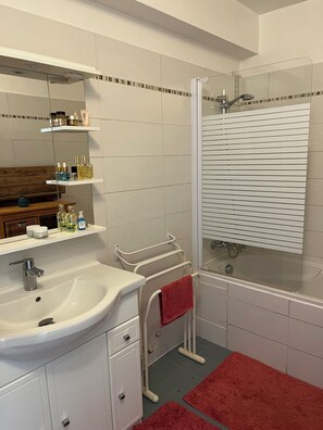 A bathroom with a sink, mirror, shower, and towel rack.