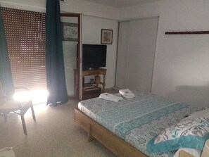 Ein Schlafzimmer mit einem Bett, einem Fernseher auf einem Holztisch, einer Tür und einem Fenster mit Jalousien.