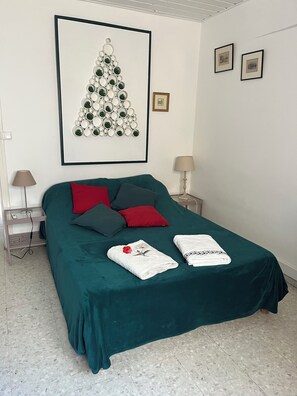 A neatly made bed with a green bedspread, two pillows, and two towels.