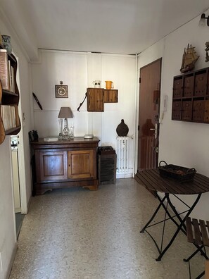 Ein schmaler Flur mit einem Holzkasten, einem kleinen Tisch und einem an der Wand befestigten Regal.