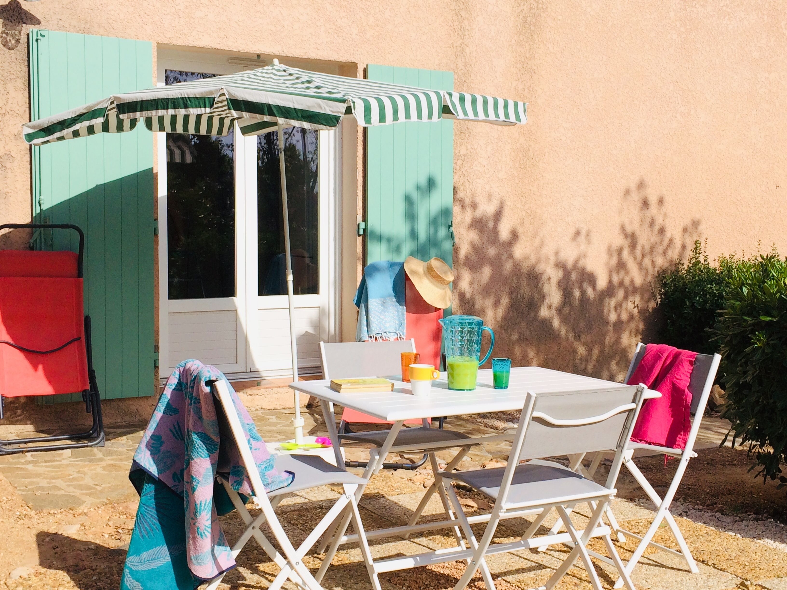 An outdoor patio with a table, chairs, a striped umbrella, and a red grill.