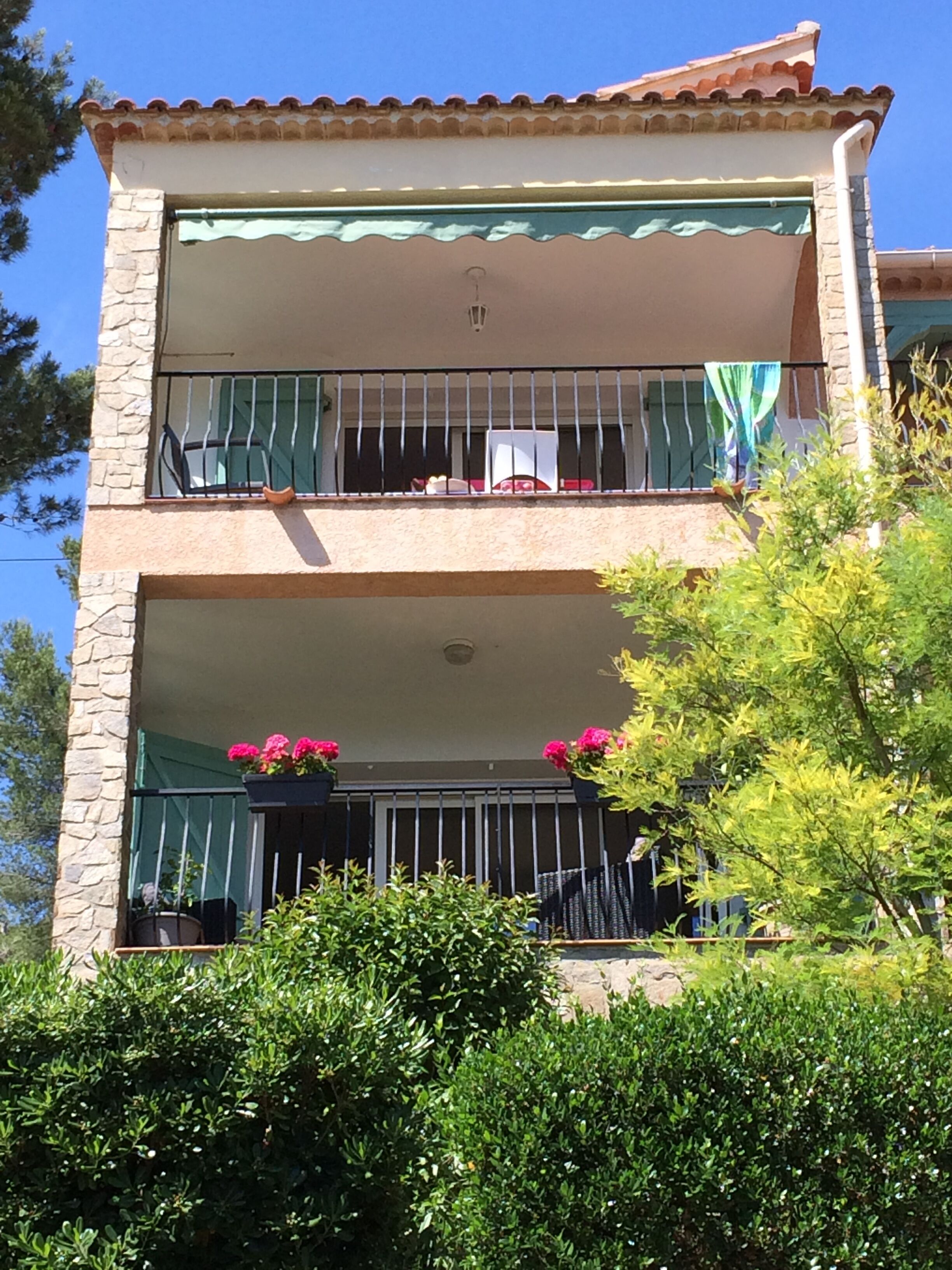 Un edificio de dos pisos con balcones, paredes de piedra y plantas en macetas.