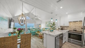 Una cocina amplia con una isla central, armarios blancos y un gran ventanal con vistas al océano.