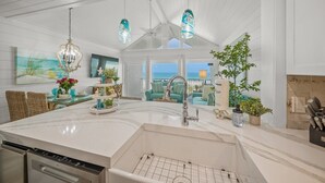 Una cocina amplia con una isla grande, modernos focos colgantes y vista al océano.
