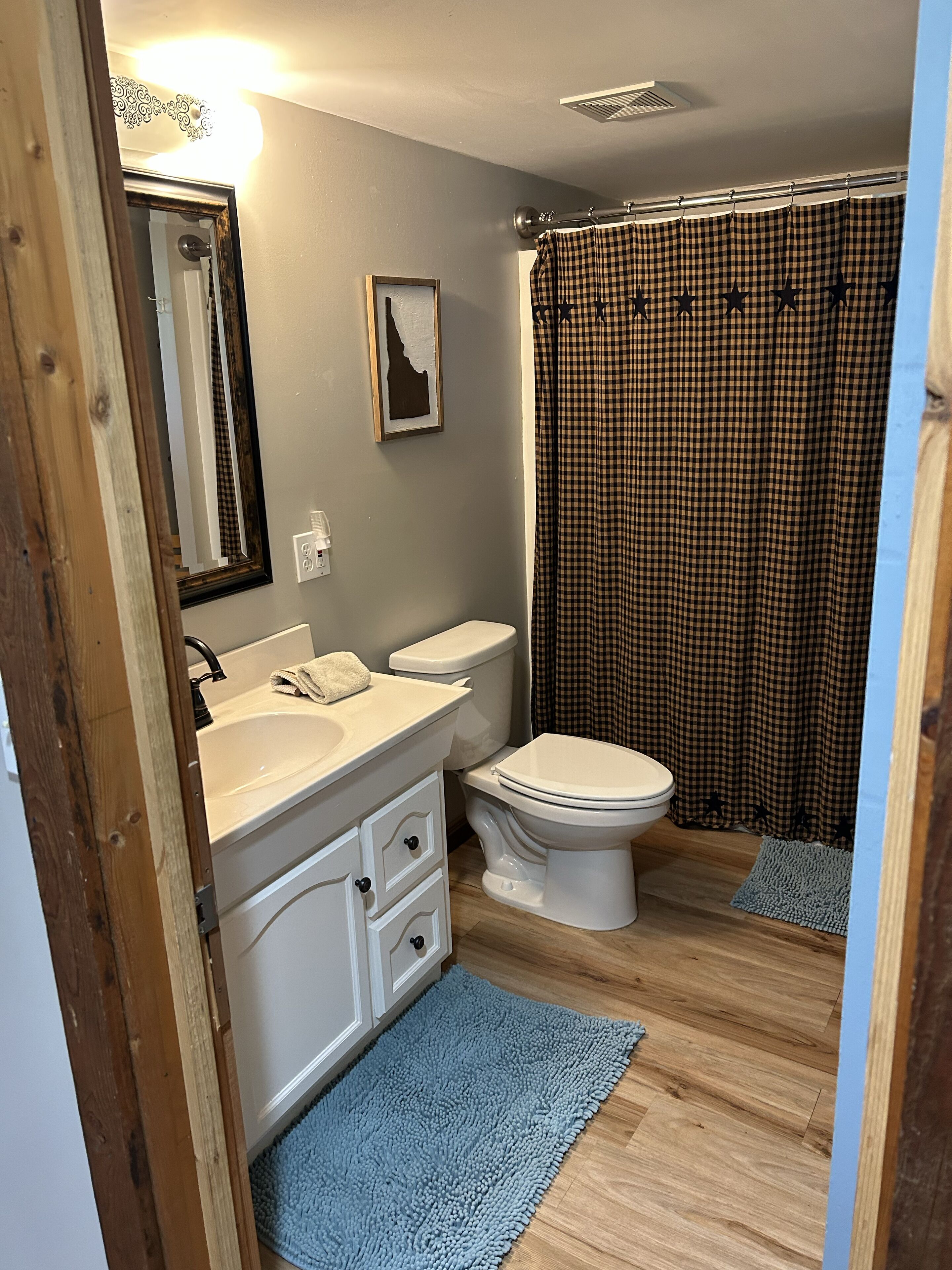 A bathroom with a white sink, a toilet, a blue rug, and a checkered shower curtain.