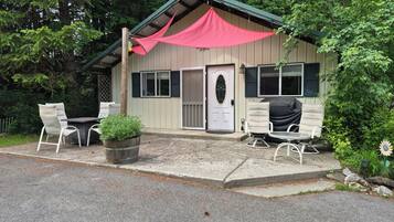 A small building with a porch, a table with chairs, and a potted plant.