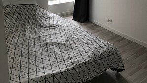 Une chambre avec une couvre-lit à motifs géométriques, une fenêtre donnant sur l’extérieur et un plafond doté d’un éclairage encastré.