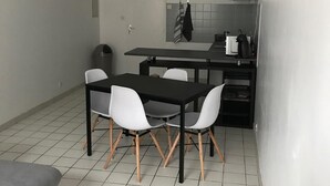 Une cuisine compacte avec un coin repas, comprenant une table noire, des chaises blanches et un canapé gris.