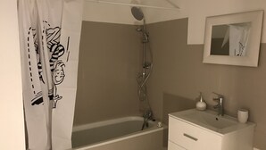 Une salle de bain avec une baignoire, une douche, un lavabo avec un miroir et un porte-serviettes.