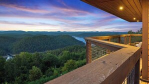 Une terrasse en bois surplombe une vallée boisée, avec une rivière et des montagnes visibles au loin.