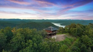 Un chalet à un seul étage, entouré d’une forêt dense, qui offre une vue sur un lac et sur des montagnes au loin.