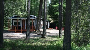 A cabin with a porch, surrounded by tall trees in a forested area.