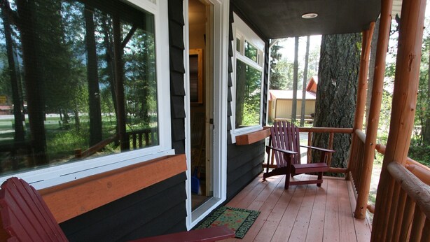 A wooden deck with two Adirondack chairs, a wooden bench, and a door leading to an interior space.