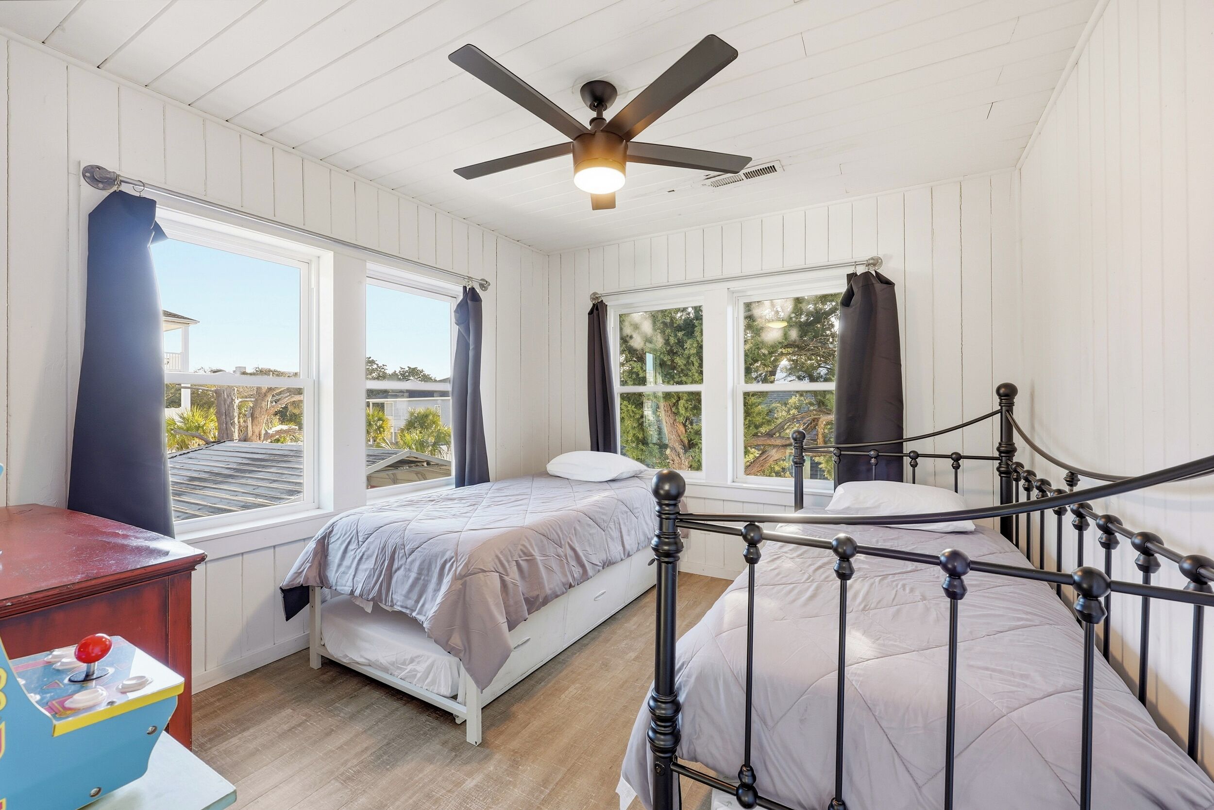 A bedroom with two beds, a ceiling fan, and large windows.