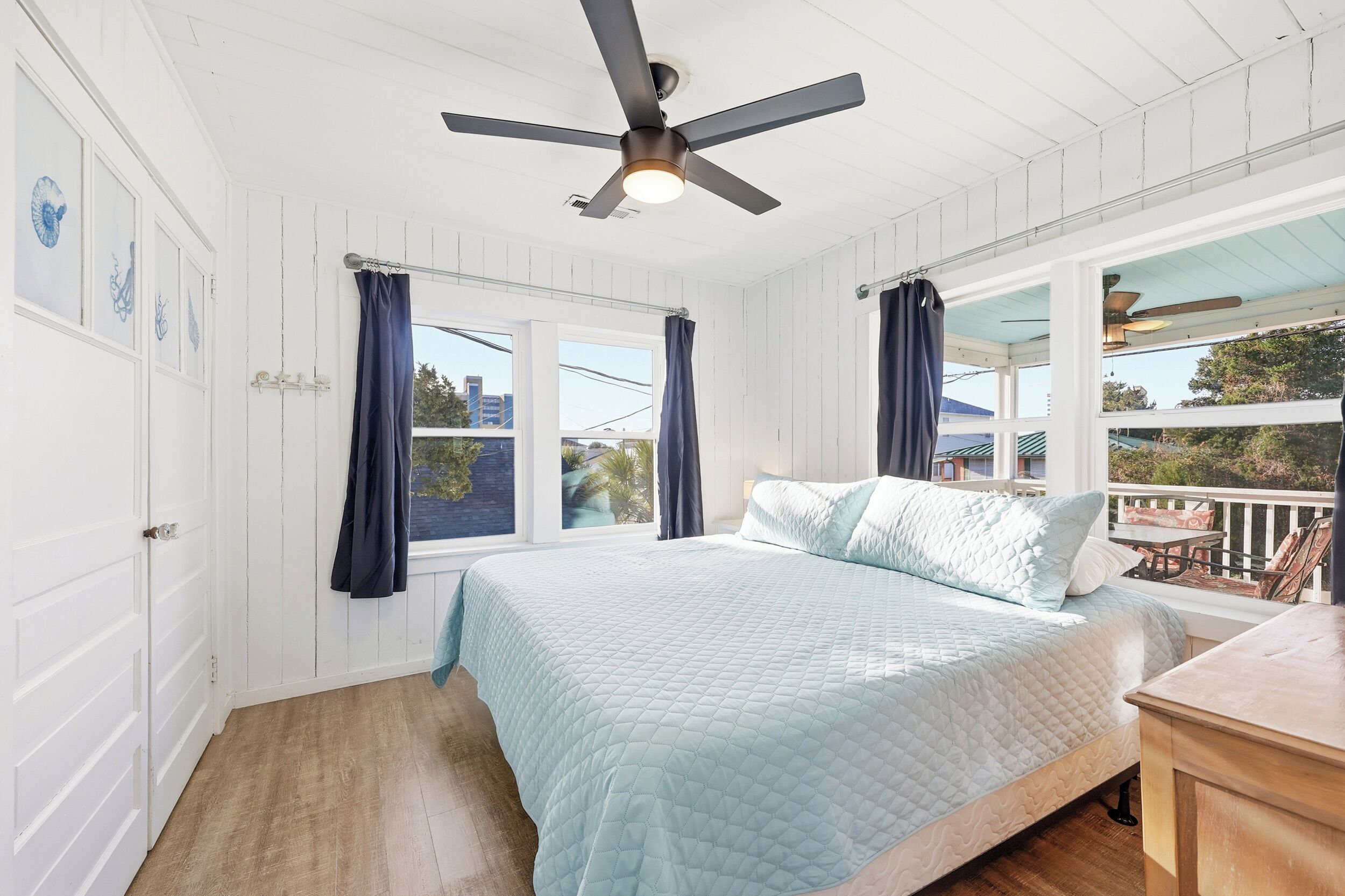 Une chambre à coucher avec un lit, un ventilateur de plafond et deux fenêtres avec des rideaux.