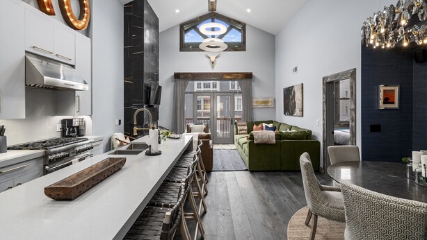A modern kitchen with a central island, a dining area with a round table, and a living room with a green sofa. - Ski In/Out and on Main Street! It Doesn't Get Any Better! (Park City)