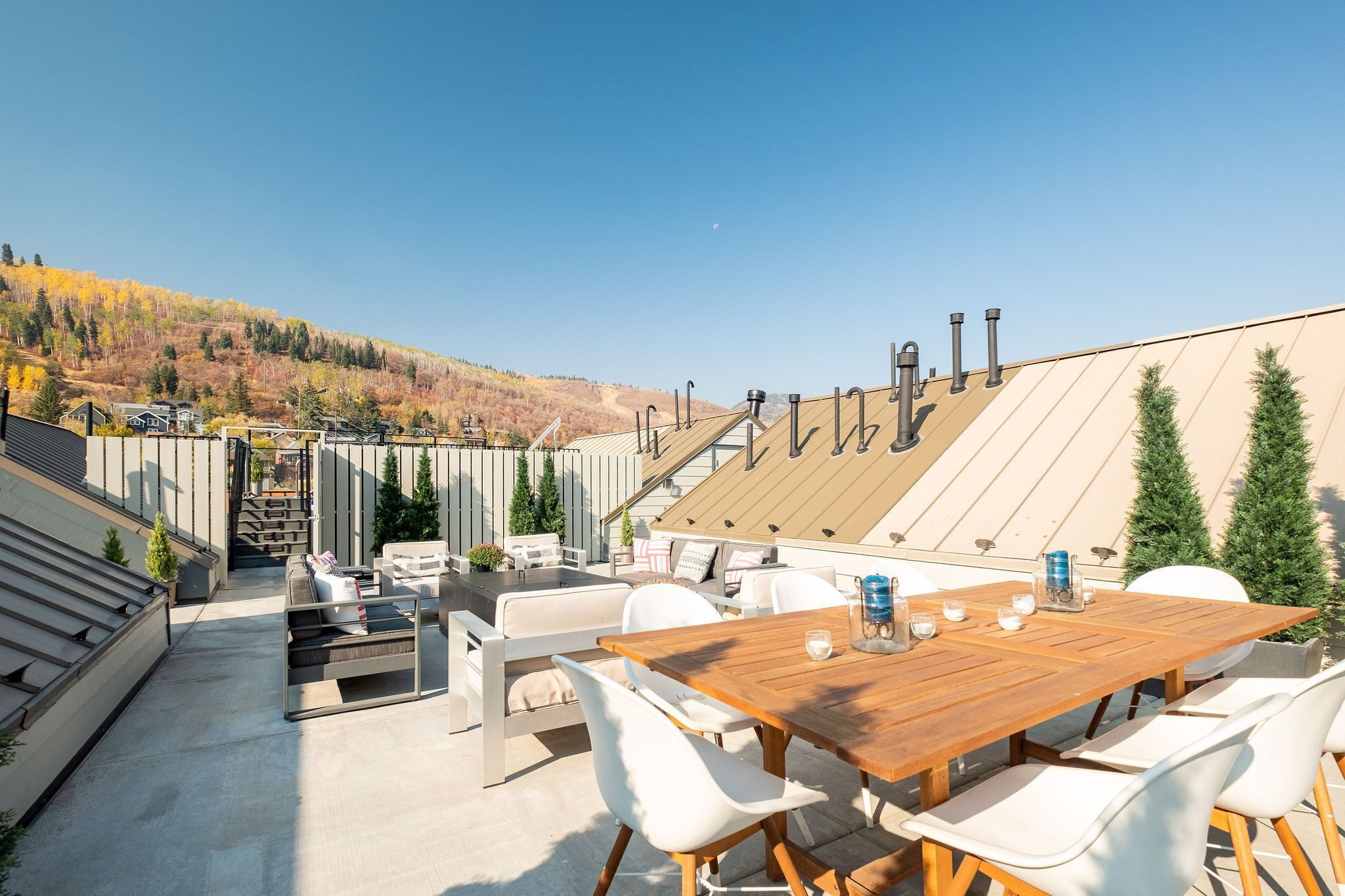 Una terrazza sul tetto con un tavolo di legno e sedie bianche, con vista su un paesaggio collinare.