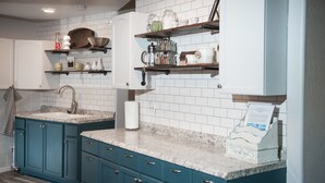 A kitchen with teal cabinets, white subway tiles, and a granite countertop. There are shelves above the sink holding jars and kitchen items. - The Bright Boho-Tel  (Flagstaff)