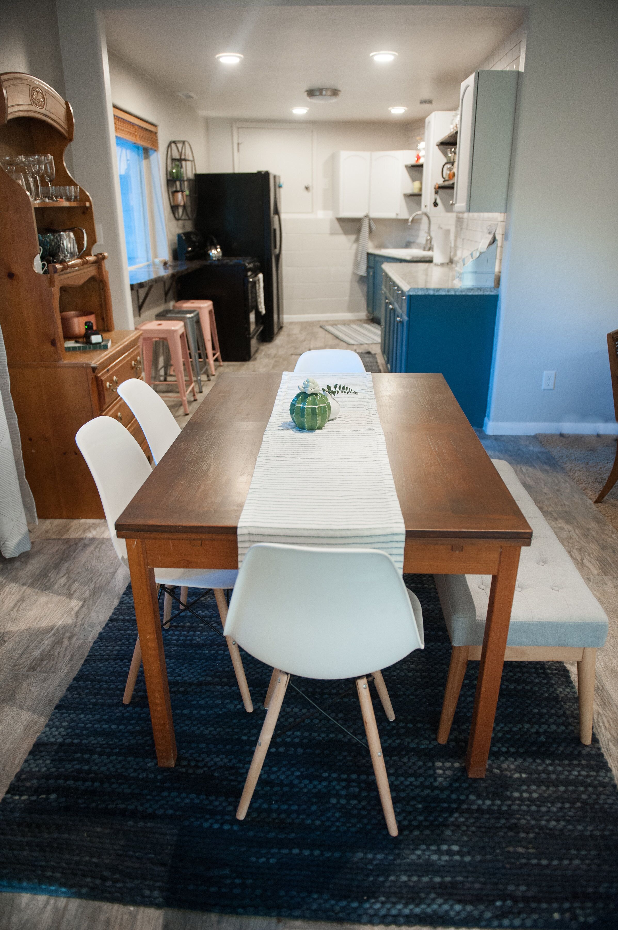 Un coin repas avec une table en bois, des chaises blanches et un tapis bleu.