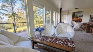 A spacious living area with a large window, white leather sofas, a wooden coffee table, and a painting on the wall. - Kirkwood Ski, Wineries, Caves, Family friendly, near Gold Country (Volcano)