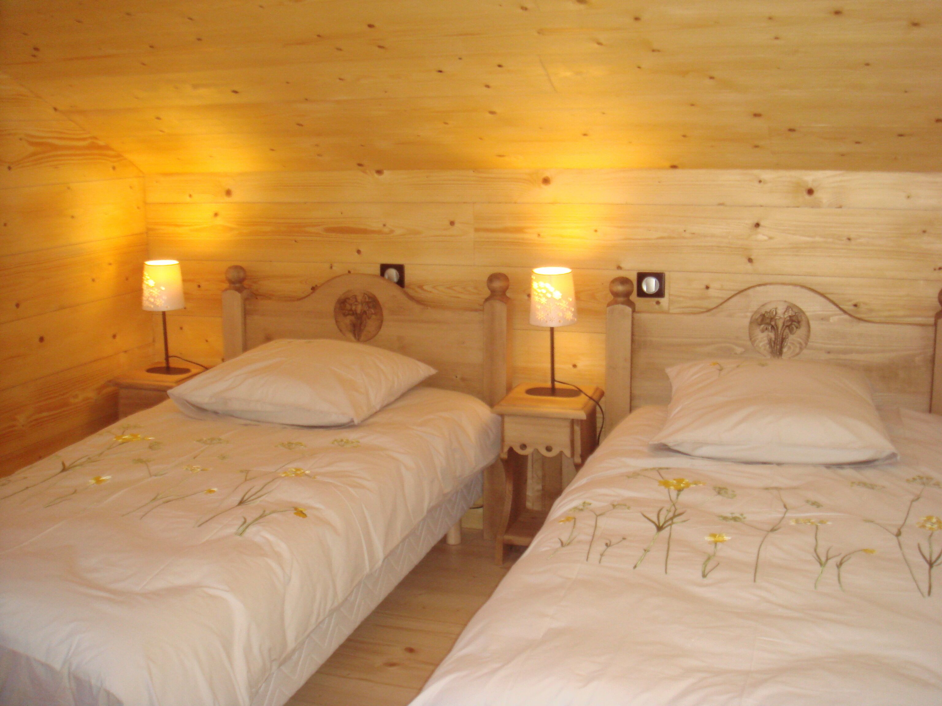 Une chambre dans un chalet en bois, avec deux lits simples, chacun doté d’une table de chevet et d’une lampe.