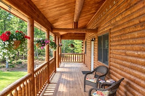 Una baita di legno con un portico coperto, sedie in vimini e cesti di fiori appesi.