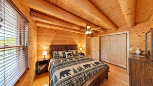 Une chambre dans un chalet en bois, comprenant un lit, des tables de chevet, un ventilateur de plafond et une armoire.