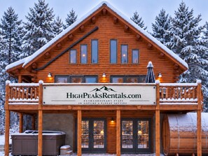 Una baita in legno con un balcone, una vasca idromassaggio e un cartello per HighPeaksRentals.com.