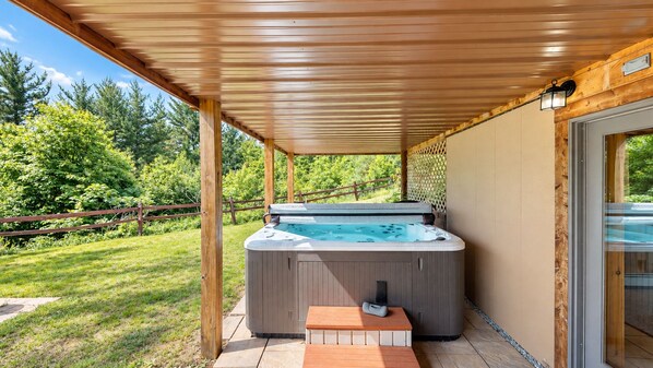 Un jacuzzi bajo una pérgola de madera con un deck de madera, rodeado por una cerca de madera y follaje.