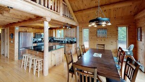 A spacious wooden cabin with a large dining table, kitchen area, and a loft with a balcony. - Grand Pines Lodge, Ultimate Log Luxury, Stunning Views, Hot Tub & Sauna, EV Charger, 3D Tour (Jay)