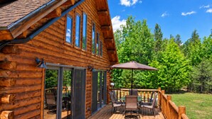 Une cabane en rondins dotée d’une terrasse, de meubles d’extérieur et offrant une vue sur la forêt environnante.