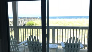 Une terrasse avec deux fauteuils Adirondack et une petite table, offrant une vue sur une plage et l’océan.