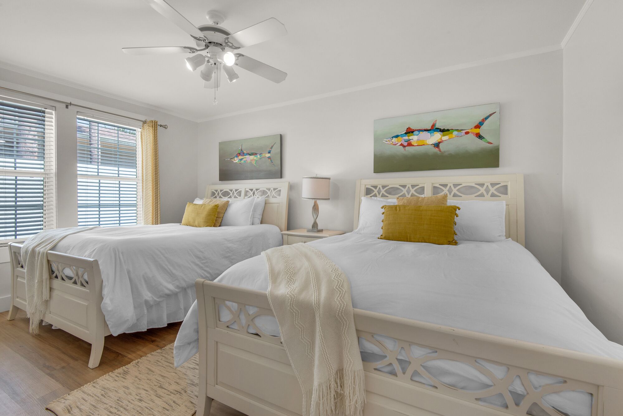 A hotel room with two beds, a ceiling fan, and artwork on the walls.