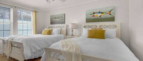 A hotel room with two beds, a ceiling fan, and artwork on the walls.