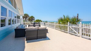 A covered outdoor seating area with wicker furniture, a white fence, and a view of the ocean.