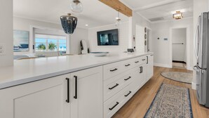 A modern kitchen with white cabinetry, a large island, pendant lighting, and a view to the outdoors.