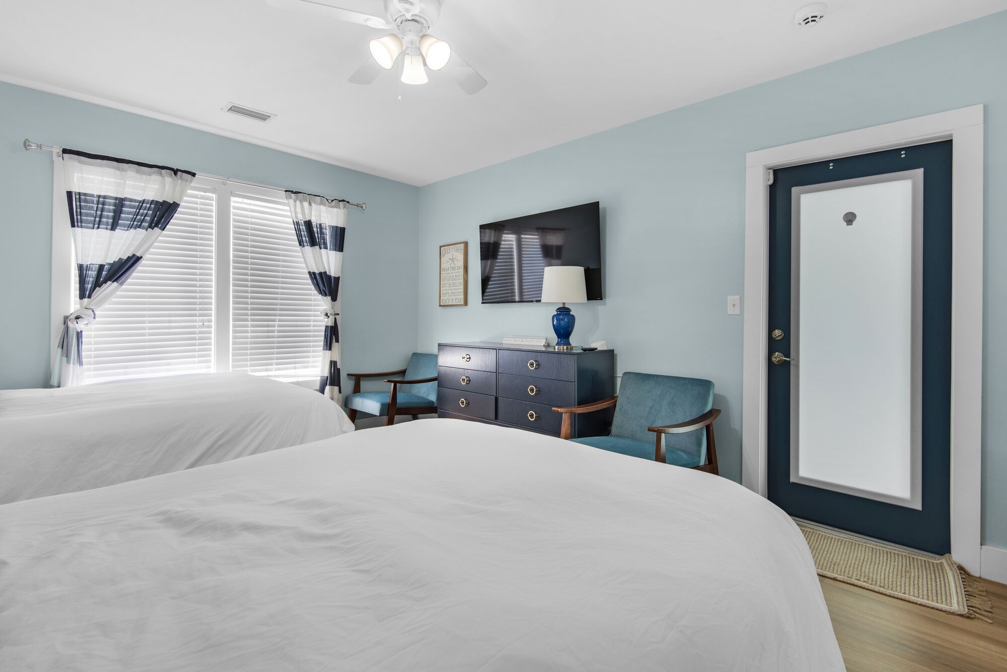 A hotel room with two beds, a dresser, a chair, a television, and a door.
