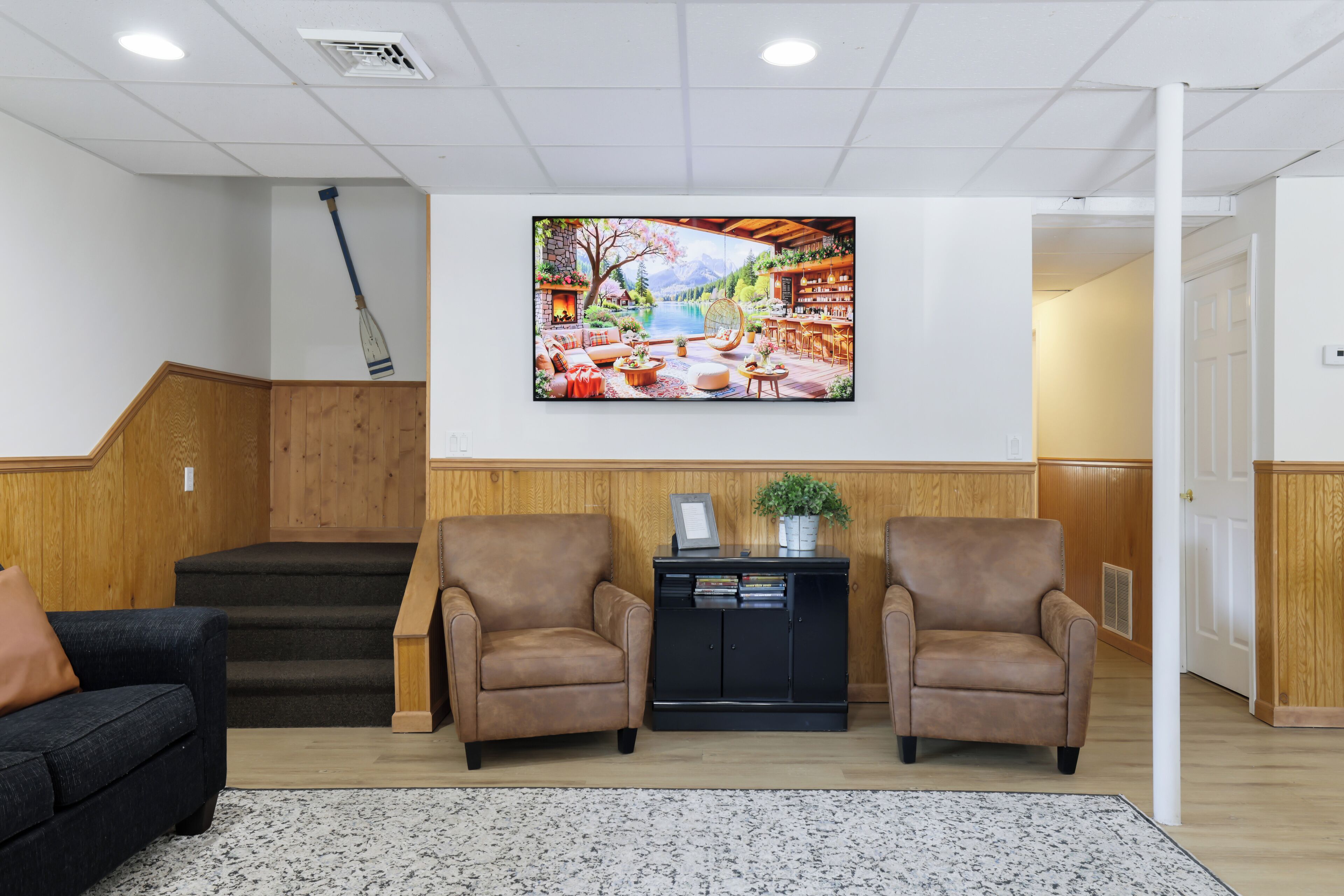 Un vestíbulo con una gran pantalla de televisión, dos sillones marrones, un mueble negro y una escalera.