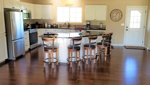 A spacious kitchen with a central island, stainless steel appliances, and wooden bar stools.